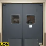 A closed PE-8000 industrial swinging door in a warehouse hallway, designed for high-impact use with reinforced bumpers and square vision panels