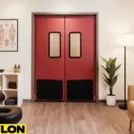 Industrial Door PE-8000 red swinging double doors inside a chiropractic and massage clinic, shown in a calming treatment space with a black therapy table, shelving with towels and oils, anatomical poster, indoor plant, and warm ambient lighting, emphasizing durability and professional design