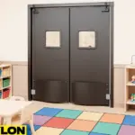 Industrial Door PE-8000 swinging double doors installed in a daycare classroom, providing safe room division with colorful foam flooring, cubbies, toys, and child-sized tables