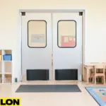 Retail Door PE-620ALC swinging door installed in a bright daycare classroom, providing safe room division with colorful cubbies, child-sized tables, and learning decorations.