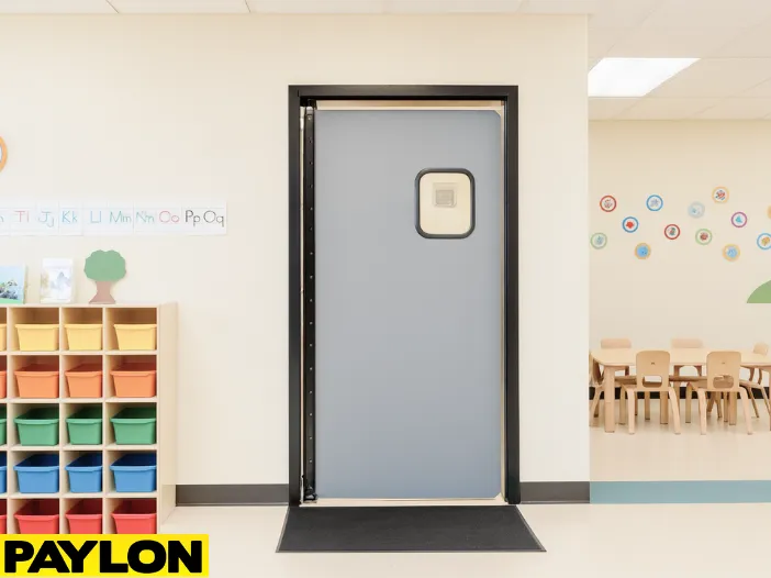 Retail Door PE-710 swinging door installed in a colorful preschool classroom, safely dividing spaces Retail Door PE-710 swinging door installed in a colorful preschool classroom, safely dividing spaces with cubbies, learning decor, and child-sized tables