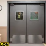 Industrial Door | PE-8000 swinging doors in a waste management facility, showing the transition from an office desk area to the warehouse floor with workers and dumpsters visible through the vision panels