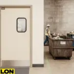 Retail Door PE-710 swinging door installed in a waste management facility, showing a clean office-to-floor transition with dumpsters and a worker in safety gear on the warehouse side
