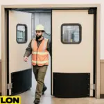 Retail Door PE-720 swinging doors in a waste management facility, with a worker in a hard hat and safety vest entering from the warehouse floor into the office area