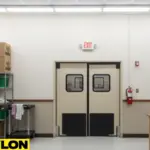 Beige commercial swinging doors in a production space with exit sign, designed for smooth and safe staff movement