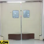 Beige restaurant swinging doors with kick plates in a prep area beside cleaning supplies and storage shelves