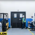 Black industrial swinging doors used in a busy factory floor with forklifts and heavy equipment nearby - Copy