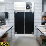 Black laminate pizza parlor swinging doors in a tiled commercial kitchen with prep tables and pizza ovens in view Black laminate pizza parlor swinging doors in a tiled commercial kitchen with prep tables and pizza ovens in view