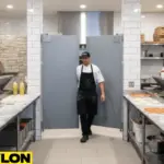 Chef walking through double gray swinging doors in a busy pizza kitchen with ovens and pizza prep tables visible Chef walking through double gray swinging doors in a busy pizza kitchen with ovens and pizza prep tables visible