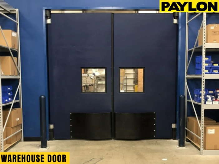 Double-swing black warehouse impact door with kick plates and vision panels in a storage facility aisle Double-swing black warehouse impact door with kick plates and vision panels in a storage facility aisle
