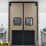 Double tan and black impact-resistant swinging doors with windows in a commercial kitchen featuring stainless-steel sinks, counters, and tiled walls Double tan and black impact-resistant swinging doors with windows in a commercial kitchen featuring stainless-steel sinks, counters, and tiled walls
