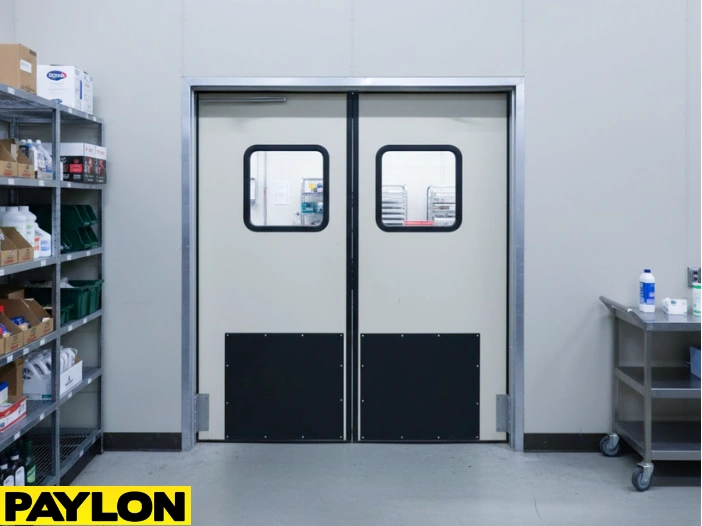 Grey double-swing warehouse impact door with clear vision panels in production facility Grey double-swing warehouse impact door with clear vision panels in production facility