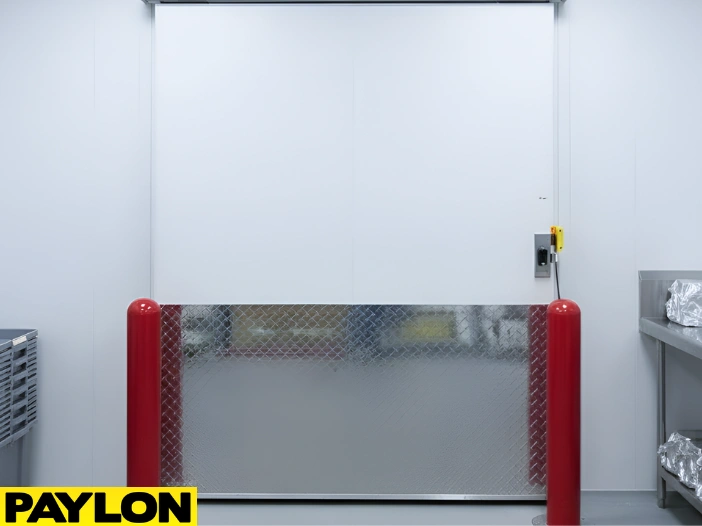 Heavy-duty sliding freezer door with diamond plate paneling and safety bollards in a cold storage room.