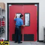 Man opening red double-swing warehouse impact door with kick plates in a storage aisle Man opening red double-swing warehouse impact door with kick plates in a storage aisle