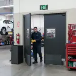 Mechanic walking through gray impact swinging doors inside an auto repair shop with tools and car lift in the background