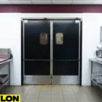 Restaurant double swinging doors in a commercial kitchen with stainless trim and black panels, showing a clean, professional food prep area
