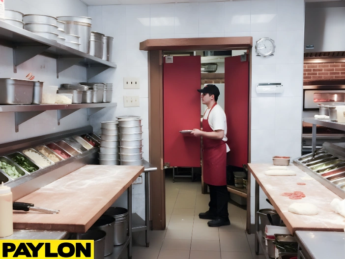 Staff member carrying a plate through red café-style swinging doors in a restaurant kitchen with pizza ingredients on the counters Staff member carrying a plate through red café-style swinging doors in a restaurant kitchen with pizza ingredients on the counter