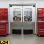 Stainless steel double swinging doors leading to a car service bay inside a mechanic workshop with tool chests nearby
