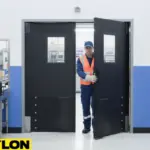 Technician walking through black double swinging factory doors in a blue-and-white assembly facility Technician walking through black double swinging factory doors in a blue-and-white assembly facility