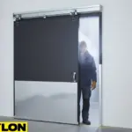 Worker entering cold storage through a black insulated sliding freezer door with diamond plate kick plate