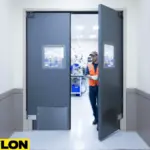 Worker entering through gray double swinging factory doors with vision panels in an industrial production area Worker entering through gray double swinging factory doors with vision panels in an industrial production area