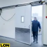 Worker opening a white insulated sliding cold storage door with small vision panel and diamond plate bottom section