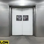 Heavy-duty white Impact Swinging Door with reinforced panels used in industrial warehouse