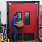 Red commercial swinging doors in a retail loading area, showing employee carrying a box through impact-resistant, high-traffic entryway