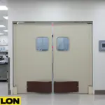 Beige double lab swinging doors with vision panels and kick plates in a busy medical lab space.