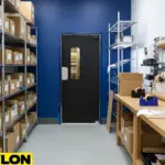 Black PE-series single swinging door in a compact packaging room with organized shelving.