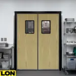 Commercial kitchen with light wood double swinging doors featuring vision panels and stainless trim, used for fast back-of-house movement.