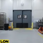 Gray industrial swinging door in a high-traffic egg handling area with carts, racks, and sanitation equipment.