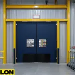 Heavy-duty dark blue swinging doors in a wide loading aisle with overhead track and cart storage in a warehouse-style factory