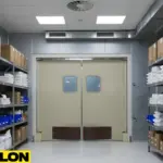 Light-colored industrial swinging doors separating a factory storage room filled with labeled bins and packaged inventory
