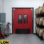 Red impact-resistant swinging doors installed between winery storage racks and production equipment.