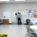 “White double swinging door in a church event room with folding chairs and bulletin board.”