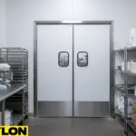 White double swinging doors with stainless lower bumpers in a commercial bakery or food prep room.