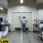 Beige double swinging doors in printing facility with staff moving materials through door, demonstrating hands-free operation