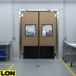 “Beige factory room swinging door with reinforced kick plates and clear vision panels for efficient internal workflow.”