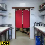 Red bar swinging doors in a commercial bar, dividing storage area from prep and service zones.