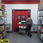 Staff member pushing a cart through red swinging doors in a busy back-of-house storage areas