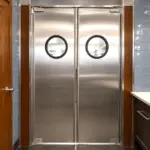 Stainless steel swinging traffic door installed in a commercial kitchen passthrough opening.