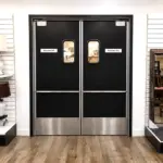 A laminate swinging door with a viewing window installed in a commercial restaurant kitchen entry.