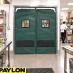 Flexible PVC swinging doors installed in an industrial facility doorway, showing impact-resistant panels.